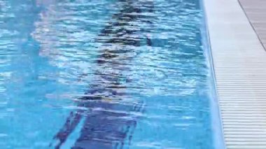 Havuzda suyun yüzeyinde küçük dalgalanmalar var. Suyun altında mavi fayanslı yüzme havuzu. Tatil teması. Arka plan olarak kullanılmak üzere su yüzeyinin videosu. Turizm kavramı, tatil