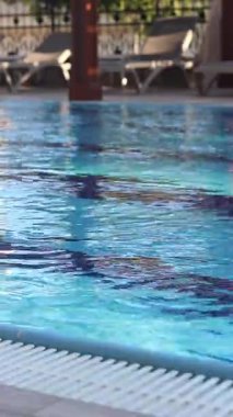 Havuzda suyun yüzeyinde küçük dalgalanmalar var. Suyun altında mavi fayanslı yüzme havuzu. Tatil teması. Arka plan olarak kullanılmak üzere su yüzeyinin videosu. Turizm kavramı, tatil