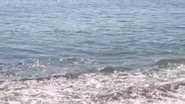 Kıyıya yakın denizde dalgalar. Deniz Burnu. Kıyıya yakın bir yerde köpüklü dalgalar salla. Plajdaki temiz su manzarası. Tatil köyünde tatil kavramı. Yaz tatilinde. Suyun üzerinde güneş parlıyor.
