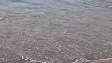 Kıyıya yakın denizde dalgalar. Deniz Burnu. Kıyıya yakın bir yerde köpüklü dalgalar salla. Plajdaki temiz su manzarası. Tatil köyünde tatil kavramı. Yaz tatilinde. Suyun üzerinde güneş parlıyor.