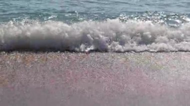 Kıyıya yakın denizde dalgalar. Deniz Burnu. Kıyıya yakın bir yerde köpüklü dalgalar salla. Plajdaki temiz su manzarası. Tatil köyünde tatil kavramı. Yaz tatilinde. Suyun üzerinde güneş parlıyor.