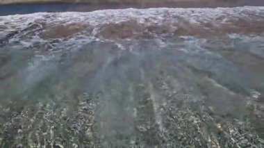 Kıyıya yakın denizde dalgalar. Deniz Burnu. Kıyıya yakın bir yerde köpüklü dalgalar salla. Plajdaki temiz su manzarası. Tatil köyünde tatil kavramı. Yaz tatilinde. Suyun üzerinde güneş parlıyor.