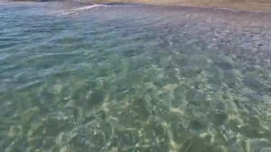 Kıyıya yakın denizde dalgalar. Deniz Burnu. Kıyıya yakın bir yerde köpüklü dalgalar salla. Plajdaki temiz su manzarası. Tatil köyünde tatil kavramı. Yaz tatilinde. Suyun üzerinde güneş parlıyor.