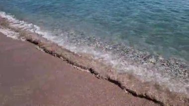 Kıyıya yakın denizde dalgalar. Deniz Burnu. Kıyıya yakın bir yerde köpüklü dalgalar salla. Plajdaki temiz su manzarası. Tatil köyünde tatil kavramı. Yaz tatilinde. Suyun üzerinde güneş parlıyor.