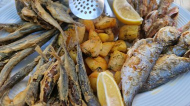 Beyaz tabakta patates ve limonlu deniz ürünleri tabağı. Tahta bir tabakta farklı balık çeşitleri var. Lezzetli ve sağlıklı yiyecekler. Patatesli kızarmış deniz balığı çeşitleri.