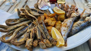 Beyaz tabakta patates ve limonlu deniz ürünleri tabağı. Tahta bir tabakta farklı balık çeşitleri var. Lezzetli ve sağlıklı yiyecekler. Patatesli kızarmış deniz balığı çeşitleri.
