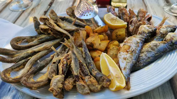 Beyaz tabakta patates ve limonlu deniz ürünleri tabağı. Tahta bir tabakta farklı balık çeşitleri var. Lezzetli ve sağlıklı yiyecekler. Patatesli kızarmış deniz balığı çeşitleri.
