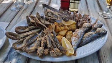 Beyaz tabakta patates ve limonlu deniz ürünleri tabağı. Tahta bir tabakta farklı balık çeşitleri var. Lezzetli ve sağlıklı yiyecekler. Patatesli kızarmış deniz balığı çeşitleri.