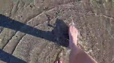 Sahilde çıplak ayakla yürüyen kadın, manzaralı. Sahil şeridi boyunca suyun üzerinde yürüyorum. Kumsal kumsalı. Tatil konsepti. Güneşli bir yaz plajında tek başına yürüyen bir kız.