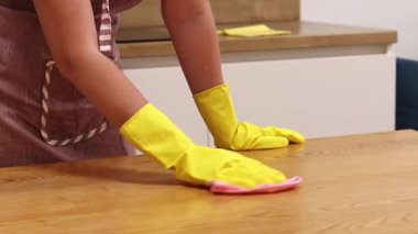 Önlüklü ve sarı eldivenli bir kadın, tozu ve toprağı yapışkan bir peçeteyle siliyor. Daireyi temizliyorum. Temizlik servisi. Ellerinizi temizleme eldivenleriyle yakın plan çekin. Temizleyici