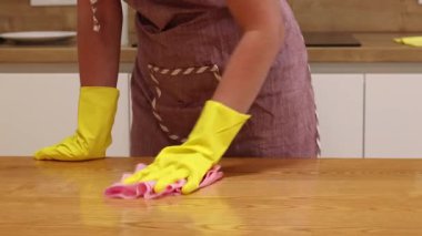 Önlüklü ve sarı eldivenli bir kadın, tozu ve toprağı yapışkan bir peçeteyle siliyor. Daireyi temizliyorum. Temizlik servisi. Ellerinizi temizleme eldivenleriyle yakın plan çekin. Temizleyici