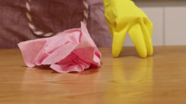 Önlüklü ve sarı eldivenli bir kadın, tozu ve toprağı yapışkan bir peçeteyle siliyor. Daireyi temizliyorum. Temizlik servisi. Ellerinizi temizleme eldivenleriyle yakın plan çekin. Temizleyici