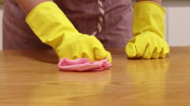 Önlüklü ve sarı eldivenli bir kadın, tozu ve toprağı yapışkan bir peçeteyle siliyor. Daireyi temizliyorum. Temizlik servisi. Ellerinizi temizleme eldivenleriyle yakın plan çekin. Temizleyici