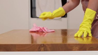 Önlüklü ve sarı eldivenli bir kadın, tozu ve toprağı yapışkan bir peçeteyle siliyor. Daireyi temizliyorum. Temizlik servisi. Ellerinizi temizleme eldivenleriyle yakın plan çekin. Temizleyici
