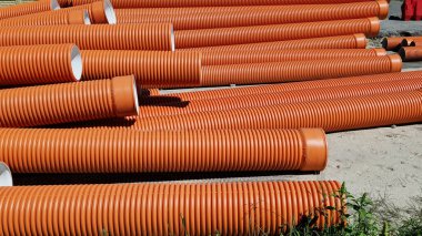 Kanalizasyon borusu, çift katmanlı. Borular üst üste yığılmış, şehirde tamirat yapılmış. Turuncu kanalizasyon boruları, yakın plan. Borular topraktan gelen değişken yüklere dayanabilir.