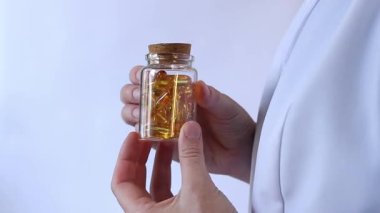 Cam kavanozu balık yağı kapsülleriyle tutan bir doktorun yakın çekimi. Omega-3. Eczacı, terapist ya da elinde ilaç olan beyaz önlüklü bir doktor. Balık yağı hapları. Tıbbi ve sağlık hizmeti kavramı