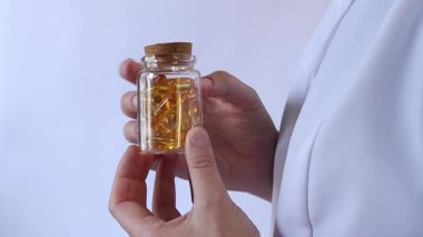Cam kavanozu balık yağı kapsülleriyle tutan bir doktorun yakın çekimi. Omega-3. Eczacı, terapist ya da elinde ilaç olan beyaz önlüklü bir doktor. Balık yağı hapları. Tıbbi ve sağlık hizmeti kavramı