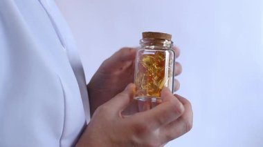 Cam kavanozu balık yağı kapsülleriyle tutan bir doktorun yakın çekimi. Omega-3. Eczacı, terapist ya da elinde ilaç olan beyaz önlüklü bir doktor. Balık yağı hapları. Tıbbi ve sağlık hizmeti kavramı