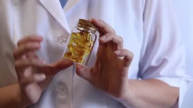 Cam kavanozu balık yağı kapsülleriyle tutan bir doktorun yakın çekimi. Omega-3. Eczacı, terapist ya da elinde ilaç olan beyaz önlüklü bir doktor. Balık yağı hapları. Tıbbi ve sağlık hizmeti kavramı
