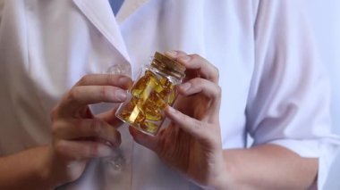 Cam kavanozu balık yağı kapsülleriyle tutan bir doktorun yakın çekimi. Omega-3. Eczacı, terapist ya da elinde ilaç olan beyaz önlüklü bir doktor. Balık yağı hapları. Tıbbi ve sağlık hizmeti kavramı