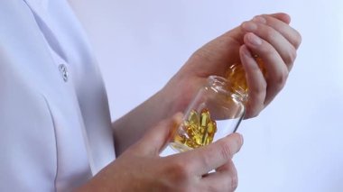 Cam kavanozu balık yağı kapsülleriyle tutan bir doktorun yakın çekimi. Omega-3. Eczacı, terapist ya da elinde ilaç olan beyaz önlüklü bir doktor. Balık yağı hapları. Tıbbi ve sağlık hizmeti kavramı