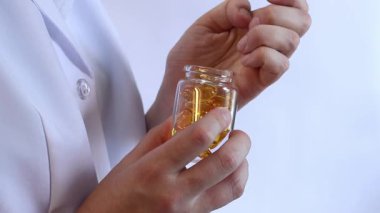 Cam kavanozu balık yağı kapsülleriyle tutan bir doktorun yakın çekimi. Omega-3. Eczacı, terapist ya da elinde ilaç olan beyaz önlüklü bir doktor. Balık yağı hapları. Tıbbi ve sağlık hizmeti kavramı