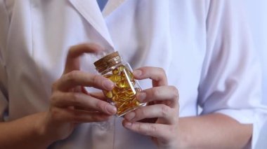 Cam kavanozu balık yağı kapsülleriyle tutan bir doktorun yakın çekimi. Omega-3. Eczacı, terapist ya da elinde ilaç olan beyaz önlüklü bir doktor. Balık yağı hapları. Tıbbi ve sağlık hizmeti kavramı