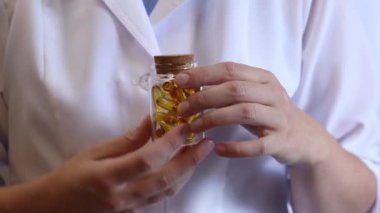 Cam kavanozu balık yağı kapsülleriyle tutan bir doktorun yakın çekimi. Omega-3. Eczacı, terapist ya da elinde ilaç olan beyaz önlüklü bir doktor. Balık yağı hapları. Tıbbi ve sağlık hizmeti kavramı