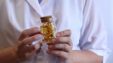 Cam kavanozu balık yağı kapsülleriyle tutan bir doktorun yakın çekimi. Omega-3. Eczacı, terapist ya da elinde ilaç olan beyaz önlüklü bir doktor. Balık yağı hapları. Tıbbi ve sağlık hizmeti kavramı