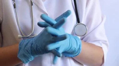 Elinde mavi tıbbi eldiven tutan bir doktorun yakın çekimi. Eczacı, terapist ya da beyaz önlüklü doktor eldiven giyiyor. Tıbbi ve sağlık hizmetleri konsepti. Bir doktorun ellerine yakın çekim