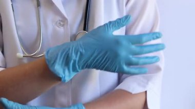 Elinde mavi tıbbi eldiven tutan bir doktorun yakın çekimi. Eczacı, terapist ya da beyaz önlüklü doktor eldiven giyiyor. Tıbbi ve sağlık hizmetleri konsepti. Bir doktorun ellerine yakın çekim