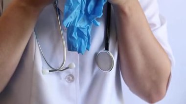 Elinde mavi tıbbi eldiven tutan bir doktorun yakın çekimi. Eczacı, terapist ya da beyaz önlüklü doktor eldiven giyiyor. Tıbbi ve sağlık hizmetleri konsepti. Bir doktorun ellerine yakın çekim