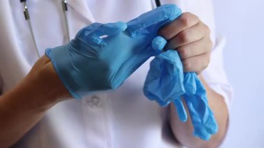 Elinde mavi tıbbi eldiven tutan bir doktorun yakın çekimi. Eczacı, terapist ya da beyaz önlüklü doktor eldiven giyiyor. Tıbbi ve sağlık hizmetleri konsepti. Bir doktorun ellerine yakın çekim