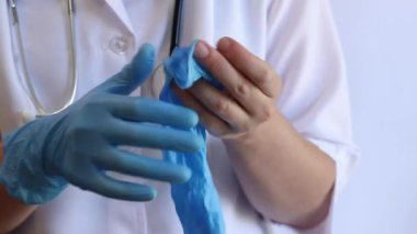 Elinde mavi tıbbi eldiven tutan bir doktorun yakın çekimi. Eczacı, terapist ya da beyaz önlüklü doktor eldiven giyiyor. Tıbbi ve sağlık hizmetleri konsepti. Bir doktorun ellerine yakın çekim