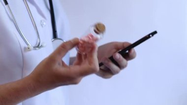 Cam kavanozda ve akıllı telefonda vitamin tutan bir doktorun yakın çekimi. Eczacı cep telefonuna bilgi yazıyor. Bir hemşirenin ellerine ilaçlarla yakın çekim.