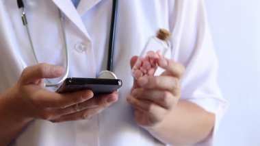 Cam kavanozda ve akıllı telefonda vitamin tutan bir doktorun yakın çekimi. Eczacı cep telefonuna bilgi yazıyor. Bir hemşirenin ellerine ilaçlarla yakın çekim.