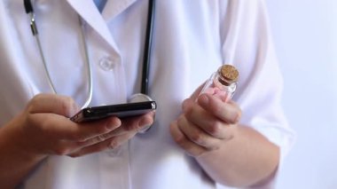 Cam kavanozda ve akıllı telefonda vitamin tutan bir doktorun yakın çekimi. Eczacı cep telefonuna bilgi yazıyor. Bir hemşirenin ellerine ilaçlarla yakın çekim.
