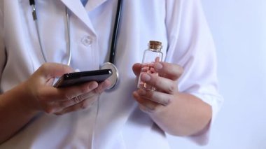 Cam kavanozda ve akıllı telefonda vitamin tutan bir doktorun yakın çekimi. Eczacı cep telefonuna bilgi yazıyor. Bir hemşirenin ellerine ilaçlarla yakın çekim.