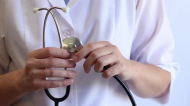 Stetoskop tutan bir doktorun yakın çekimi. Bir hemşirenin ellerine steteskopla yakın çekim, beyaz önlüklü bir doktor veya terapist. Sağlık ve tıp konsepti. Tıbbi aletli bir terapist.