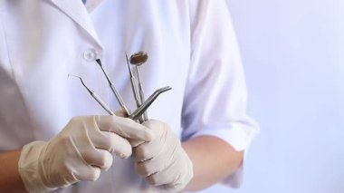 Diş aletini tutan bir doktorun ellerinin yakın çekimi. Diş aynası olan bir dişçi, kavisli forseps ve ellerinde diş kancası. İlaçlar. Sağlık sigortası konsepti. Beyaz önlüklü doktor.