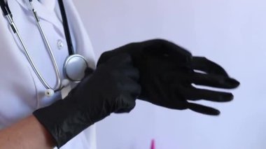 Elinde siyah tıbbi eldiven tutan bir doktorun yakın çekimi. Eczacı, terapist ya da beyaz önlüklü doktor eldiven giyiyor. Tıbbi ve sağlık hizmetleri konsepti. Bir doktorun ellerine yakın çekim