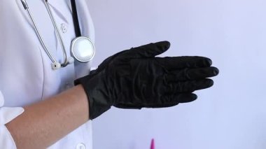 Elinde siyah tıbbi eldiven tutan bir doktorun yakın çekimi. Eczacı, terapist ya da beyaz önlüklü doktor eldiven giyiyor. Tıbbi ve sağlık hizmetleri konsepti. Bir doktorun ellerine yakın çekim