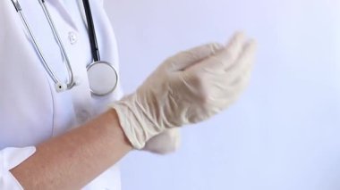 Elinde beyaz tıbbi eldiven tutan bir doktorun yakın çekimi. Eczacı, terapist ya da beyaz önlüklü doktor eldiven giyiyor. Tıbbi ve sağlık hizmetleri konsepti. Bir doktorun ellerine yakın çekim