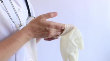 Elinde beyaz tıbbi eldiven tutan bir doktorun yakın çekimi. Eczacı, terapist ya da beyaz önlüklü doktor eldiven giyiyor. Tıbbi ve sağlık hizmetleri konsepti. Bir doktorun ellerine yakın çekim