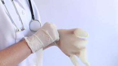 Elinde beyaz tıbbi eldiven tutan bir doktorun yakın çekimi. Eczacı, terapist ya da beyaz önlüklü doktor eldiven giyiyor. Tıbbi ve sağlık hizmetleri konsepti. Bir doktorun ellerine yakın çekim