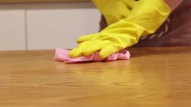 Odayı temizliyorum. Önlük giymiş tanınmayan bir kadın ve eldivenler masanın tozunu ve pisliğini temizler. Sarı eldivenli eller yakın plan. Kadın, masayı yapışkan bir bezle siler. Temizlik servisi