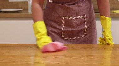 Odayı temizliyorum. Önlük giymiş tanınmayan bir kadın ve eldivenler masanın tozunu ve pisliğini temizler. Sarı eldivenli eller yakın plan. Kadın, masayı yapışkan bir bezle siler. Temizlik servisi