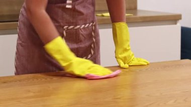 Odayı temizliyorum. Önlük giymiş tanınmayan bir kadın ve eldivenler masanın tozunu ve pisliğini temizler. Sarı eldivenli eller yakın plan. Kadın, masayı yapışkan bir bezle siler. Temizlik servisi