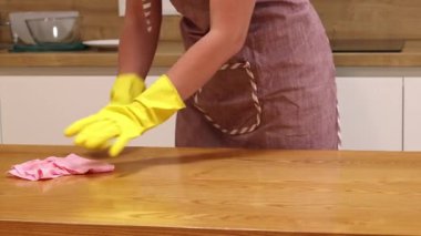 Odayı temizliyorum. Önlük giymiş tanınmayan bir kadın ve eldivenler masanın tozunu ve pisliğini temizler. Sarı eldivenli eller yakın plan. Kadın, masayı yapışkan bir bezle siler. Temizlik servisi