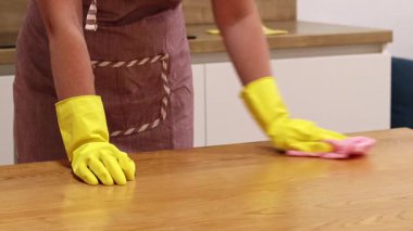 Odayı temizliyorum. Önlük giymiş tanınmayan bir kadın ve eldivenler masanın tozunu ve pisliğini temizler. Sarı eldivenli eller yakın plan. Kadın, masayı yapışkan bir bezle siler. Temizlik servisi